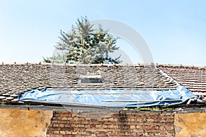 Damaged roof with tiles on the old house covered with plastic nylon to protect interior from rain water