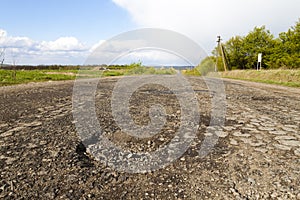 Damaged rural road, cracked asphalt blacktop with potholes and p