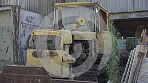 Damaged rusty tractor standing on abandoned ruins of factory. Neglected ruined machinery outdoors. Old industrial