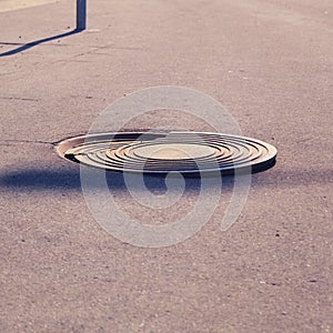 Damaged sewer manhole on the asphalt path, broken metal cover close-up