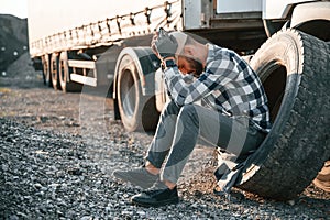 Damaged tire. Young truck driver is with his vehicle at daytime