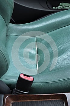 Damaged, torn, or cracked leather seat cover. Bruised old green car seat leather ripped along the seam, no people