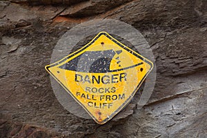 Damaged warning sign of falling rocks at cliff