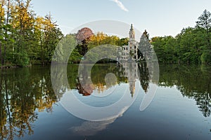 Dammsmuhle Castle in the middle of a serene lake surrounded by lush green trees in the distance