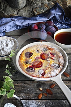 Damson blue plum clafoutis flan and cup of tea, icing sugar and almonds dressing