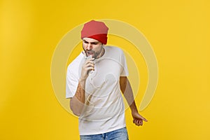 Dance. Handsome young stylish man in headphones holding mobile phone and dancing while standing against yellow