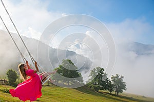 Dance of joy in the air by a girl in a pink dress on a swing