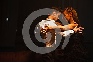 Dance and love concept. Young couple in elegant evening dresses posing in the room filled with dramatic light. Two