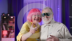 dance party, portrait of cheerful old man in glasses with an elderly woman with pink hair having fun among flying