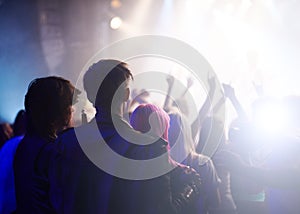 Dance, rock and friends in crowd at music festival from back, watching live band performance on stage. Audience in arena