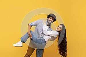 Dance together on romantic date. Happy indian man and woman hugging, smiling at camera on yellow background