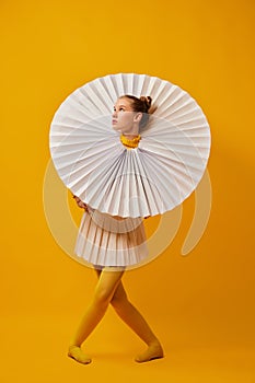 Dance. Young indifferent girl in giant jabot collar or neckwear and yellow tights isolated over yellow background