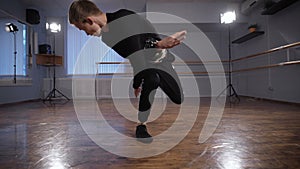 Dancer in black shirt and trousers showing modern breakdancing in classroom with mirrors and ballet barre. Young man is