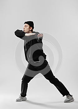 Dancer dressed in black jeans, sweatshirt, hat and gray sneakers is dancing making movements with his hands in the