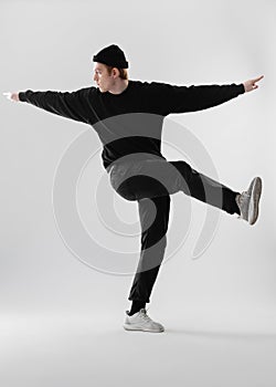 Dancer dressed in black jeans, sweatshirt, hat and gray sneakers is dancing making movements with his legs in the studio