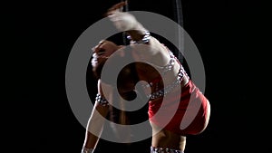 Dancer female balancer in beige leotard back lying hang on aerial hoop on black background. Slow motion. Close up