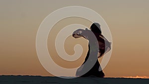 Dancer holds a veil in her hands, she dances a belly dance on the beach. Silhouette