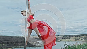 Dancer spin on pole outdoors. Pole dance practice. Female in red.