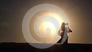 Dancer with a veil in her hands dancing belly dance on the beach. Silhouette. Slow motion