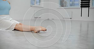 Dancer warms up her legs before rehearsal on the floor of white dance hall, ballet dancer, ballerina in the ballet