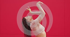 Dancing beautiful girl perform passionate dance on red background. Female professional graceful dancer cool moving hands