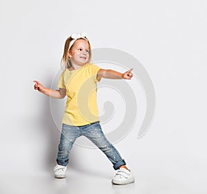 Dancing boogie cool playful kid baby girl in yellow t-shirt is having fun good time pointing at us feeling great