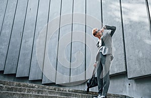 Dancing, celebrating success. Young businessman in grey formal wear is outdoors in the city