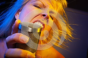 Dancing female vocalist under gelled lighting sings with passion into condenser microphone