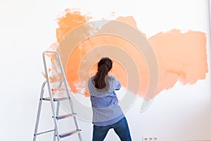 Dancing funny woman painting interior wall of home with paint roller. Redecoration, renovation, apartment repair and