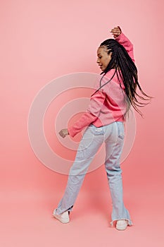 Studio shot of young excited girl with afro hairdo in casual style outfit having fun isolated on pink background