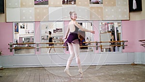 In dancing hall, Young ballerina in purple leotard performs tour jete en dedans, She is moving through the ballet class