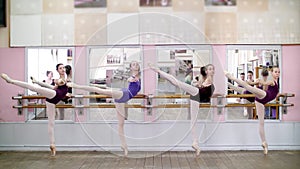 in dancing hall, Young ballerinas in purple leotards perform attitude efface on pointe shoes, standing near barre at photo