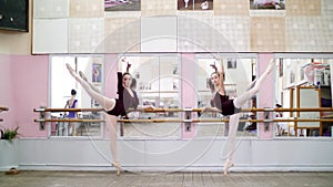 in dancing hall, Young ballerinas in purple leotards perform grand battement back on pointe shoes, raise their legs up
