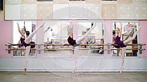 in dancing hall, Young ballerinas in purple leotards perform grand battement back on pointe shoes, raise their legs up