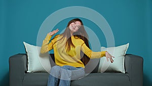 Dancing happy young girl having fun, celebrating win, enjoying music, sitting on sofa. Funny optimistic victory dance