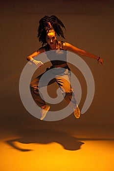 Dancing mixed race girl jumping and levitating in warm studio light. Female dancer performer jump in hip hop dance