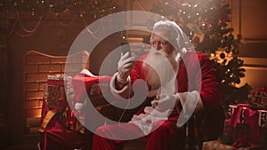 Dancing Santa Claus with headphones and a mobile phone in his hands. Listen to music online. Jerky and dynamic songs