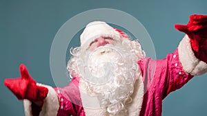 Dancing Santa Claus with red nose on blue studio background in red gloves with a white lush beard.