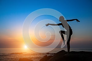 Dancing silhouette of young woman on the sea coast during sunset.