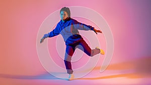 Dancing style. Black lady making hip-hop tricks on gradient pink neon background, panorama, full length