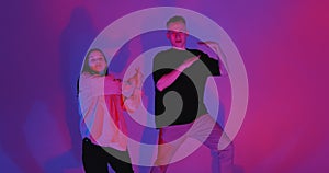 Dancing young couple quickly moving in colorful neon studio light. Contemporary dance, hip hop dancers performance
