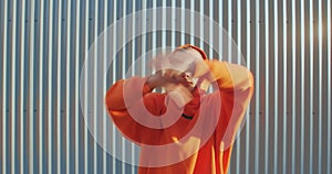 Dancing young lgbt man wearing hoodie performing expressive dance hands movements outdoors on street fence background