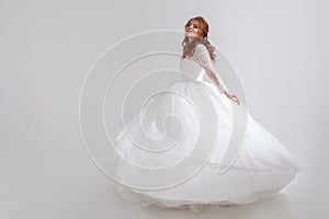 Dancing young woman in wedding dress. Charming bride on Light background.