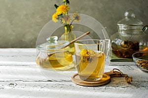 Dandelion honey and tea on the white wooden table with tea pot, dandelion flowers, dry herbal mix for infusion