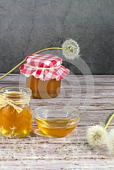 Dandelion jam, honey, jelly in a glass jar on a wooden table, black background with fresh flowers, dandelion airy seed