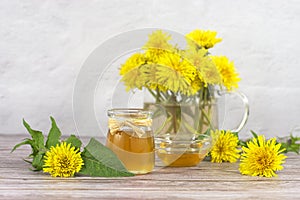 Dandelion jam, honey, jelly in a glass jar on a wooden table, white background with fresh yellow dandelion flowers