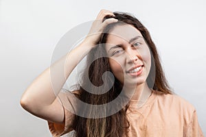 Dandruff and lice. Portrait of a young Caucasian brunette woman in a beige t-shirt, who strongly scratches her head with her hand