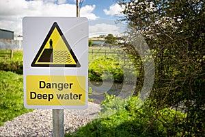 Danger Deep Water warning sign close up by rural waterway river stream. Beware falling in, drowning.