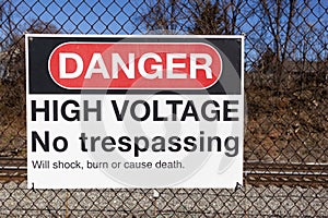 Danger, high voltage, no trespassing sign on a fence in front of a rail road