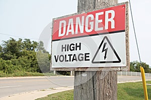 danger high voltage sign on wood post with bridge road behind, red white black. p